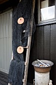 Fischernetz auf Holzleiter drapiert, seitlich Topf mit Muschelschalen auf zylindrischer Ablage, vor Hauswand