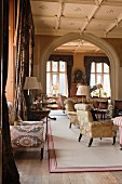 Antique side tables and armchairs with silk damask and ikat upholstery in grand salon with stucco ceiling and Tudor arch