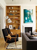 Fifties-style black armchairs with wooden frames in front of wooden fitted shelves in niche in living room
