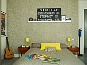 Dopppelbett mit Bettwäsche in Taupe, seitlich gelbe Tischleuchten auf filigranem Nachtkästchen, an tapezierter Wand