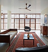 Sitzgruppe mit Retro Ledersesseln und puristischem Holzsofa auf Orientteppich; gedämpftes Licht durch Fensterfront mit Sonnenschutz