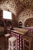 Kitchen counter with gingham-curtained base and wooden bar stools in old house with limestone walls and vaulted ceiling