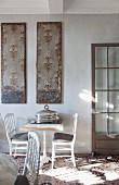 Bistro table and two chairs against wall below vintage painted panels