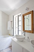 Washstand with twin sinks on white base unit below mirror with pale wooden frame