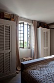 Wardrobes with louver doors flanking lattice window in bedroom