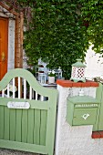 Green-painted wooden garden gate next to wall matching green post box mounted on garden wall