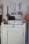 White enamel bread bin on rustic cabinet below rack of ladles
