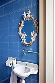 Nostalgisches Waschbecken vor blauer Fliesenwand und romantischer Porzellan-Spiegelrahmen in Vintage-Ambiente