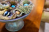 Osternest aus Stroh mit bunt bemalten Eiern in Keramikschale