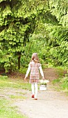 Little girl carrying basket of lily-of-the-valley along woodland path