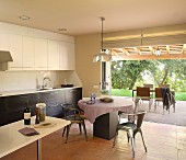 Retro Metallstühle um rundem Tisch in offener Küche vor Terrasse mit Gartenblick