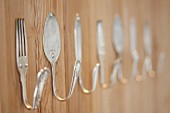 Antique, silver cutlery bent into hooks on wooden wall