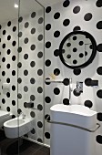 Designer Waschbecken vor schwarz-weiss gepunkteter Wand, seitlich Glas Trennscheibe vor Bidet und Toilette