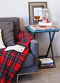 Tartan blanket on couch next to glass of wine and stacked books on folding table