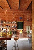 Bar stool with copper seat at breakfast counter in loft-apartment kitchen; open-fronted metal shelving and blackboard on brick wall