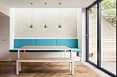 Modern table and matching bench in front of masonry bench with blue cushions below row of brass pendant lamps