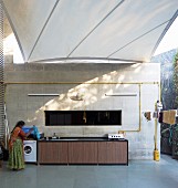 Awning shading spacious terrace; woman standing next to washing machine in outdoor kitchen counter