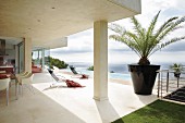 Designer dining area below projecting concrete roof and sun loungers on pool terrace of modern holiday home by the sea