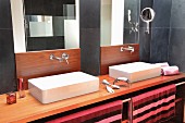 Designer-style twin washstand with wooden elements, charcoal-grey tiles and brightly stripes towels on stainless steel rail