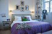 Purple cover on double bed with wooden headboard below framed photos on wall