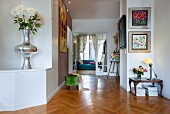 Herringbone parquet floor, tall silver vase of chrysanthemums and open double doors in background in hallway of period apartment
