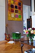 Vase of roses on antique side table and green velvet pouffe below modern artwork on painted wall
