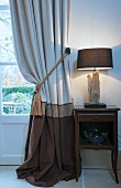 Curtain in shades of brown next to lamp on bedside table