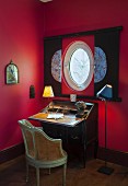 Antique writing desk below porthole window in red wall