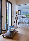 Low sideboard on castors, industrial-style tripod lamp and view into kitchen-dining room