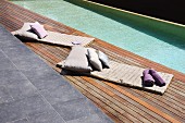 Quilted mats with cushions on wooden deck adjoining modern pool