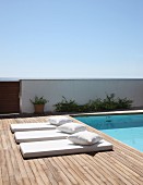 Pale futon loungers with matching cushions on wooden deck adjoining pool