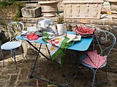 Pans and lids, wild asparagus and basket of tomatoes on pastel blue terrace table