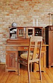 Biedermeier chair at antique writing desk against exposed brick wall