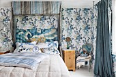 Half-tester double bed with upholstered headboard and blue and grey striped canopy in bedroom with blue floral wallpaper