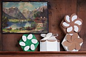 Hexagonal folded gift boxes with floral rosettes on narrow window ledge below traditional landscape painting on wood-panelled wall