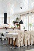 Chairs with loose, laced covers in dining area in open-plan kitchen with black extractor hood above counter