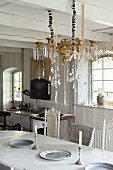 Brass chandelier with glass pendants suspended above dining table from white wooden ceiling