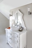 Vintage chest of drawers with modern countertop sink and carved vanity mirror painted white in modern, attic bathroom painted pale grey