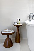Two-part set of wooden side tables with marble tops against pale grey wall tiles in modern bathroom
