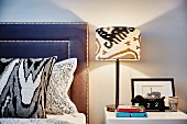 Table lamp on bedside table, bed with scatter cushions and headboard upholstered in blue leather