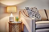 Table lamp on cylindrical, hand-crafted side table next to beige sofa with scatter cushion
