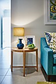 Bowl of fruit and table lamp on round, wooden side table next to pale blue couch
