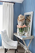 Easy chair next to tailors' dummy, mirror and vase of roses on vintage tray table against elegant striped wallpaper
