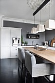 Upholstered chairs with pale grey covers at wooden table below three pendant lamps in kitchen-dining room