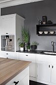 Island counter with wooden worksurface opposite kitchen counter with white base units against grey-painted wall