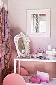 Mirror and cosmetics on serving trolley used as dressing table against pink-painted wall