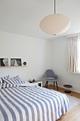 Doppelbett mit gestreifter Bettwäsche, seitlich Retro Stuhl in modernem Schlafzimmer, Pendelleuchte mit Papierschirm