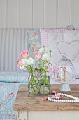 Ranunculus in glass bottles in wore frame, bead heart and glass cover on cake stand on old table in front of sofa