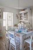 Shabby-chic table with pastel place settings, old kitchen chairs and antique white dresser in background