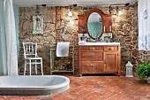 Spacious bathroom with sunken bathtub in terracotta floor, rustic washstand and stone wall